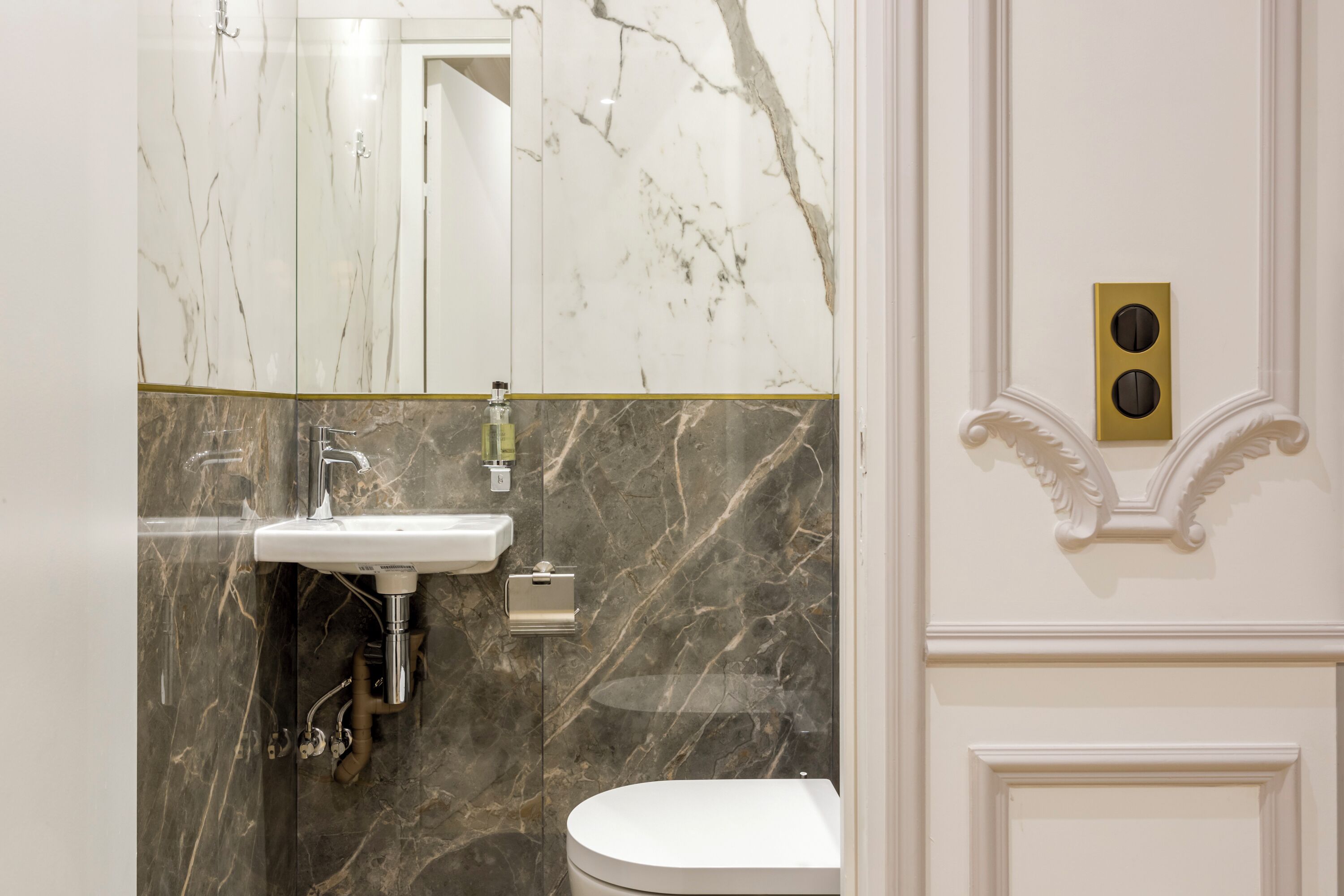 A bathroom with a marble wall, a sink, a toilet, and a mirror.
