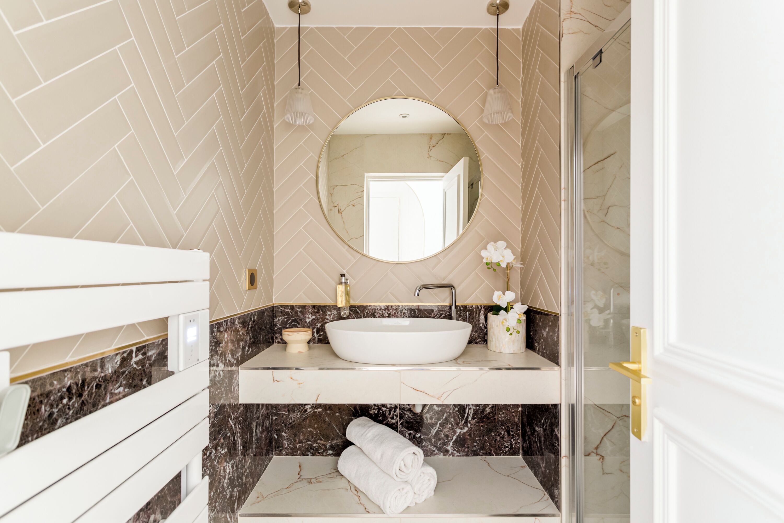A bathroom with a white sink, marble backsplash, and a round mirror.