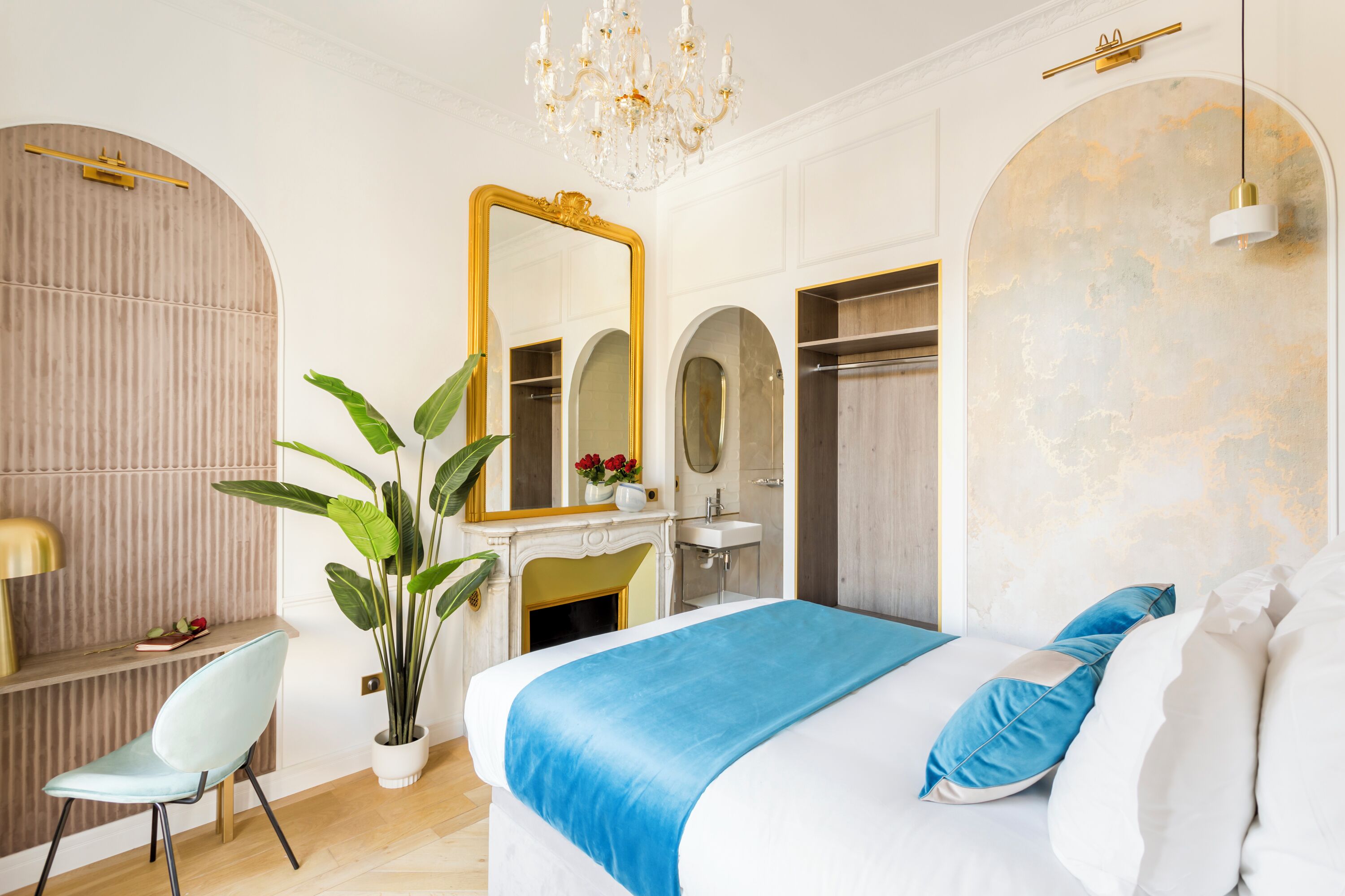 A modern bedroom with a large bed, a vanity with a mirror, a chandelier, and a potted plant.