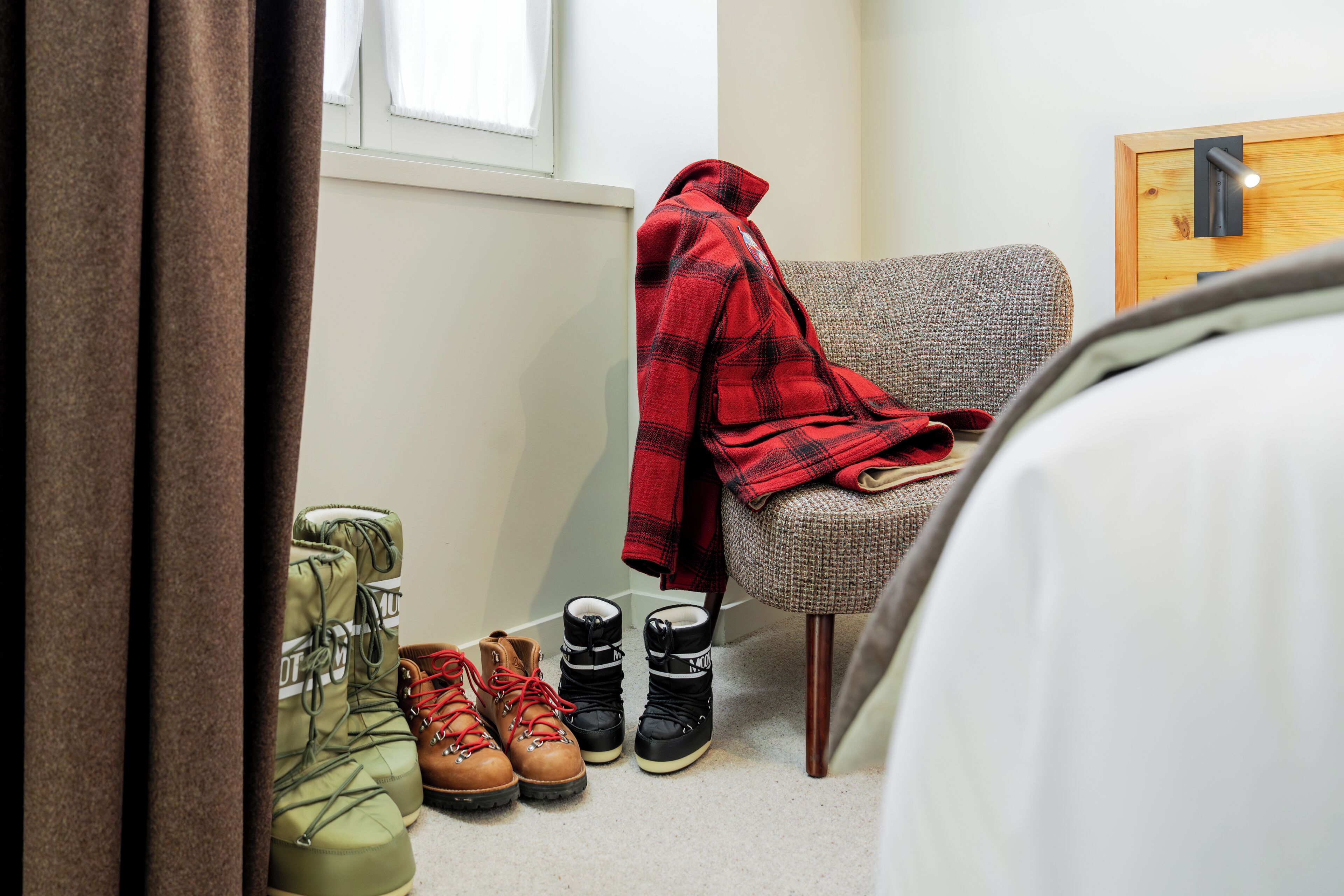 Um quarto com uma cadeira, um cobertor e um par de botas.