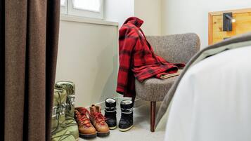 Um quarto com uma cadeira, um cobertor e um par de botas.