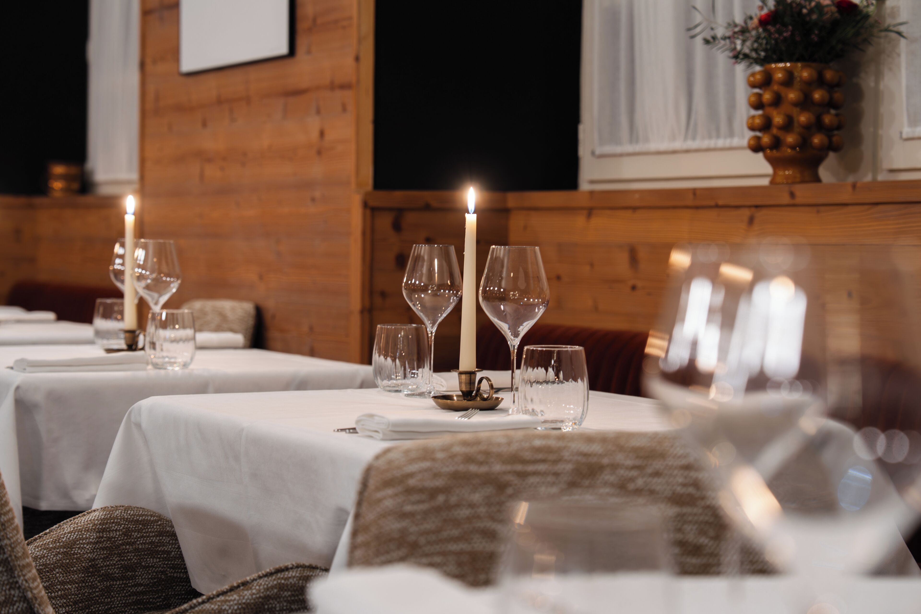 Comedor con mesas dispuestas para dos, cada una con una vela y copas de vino.