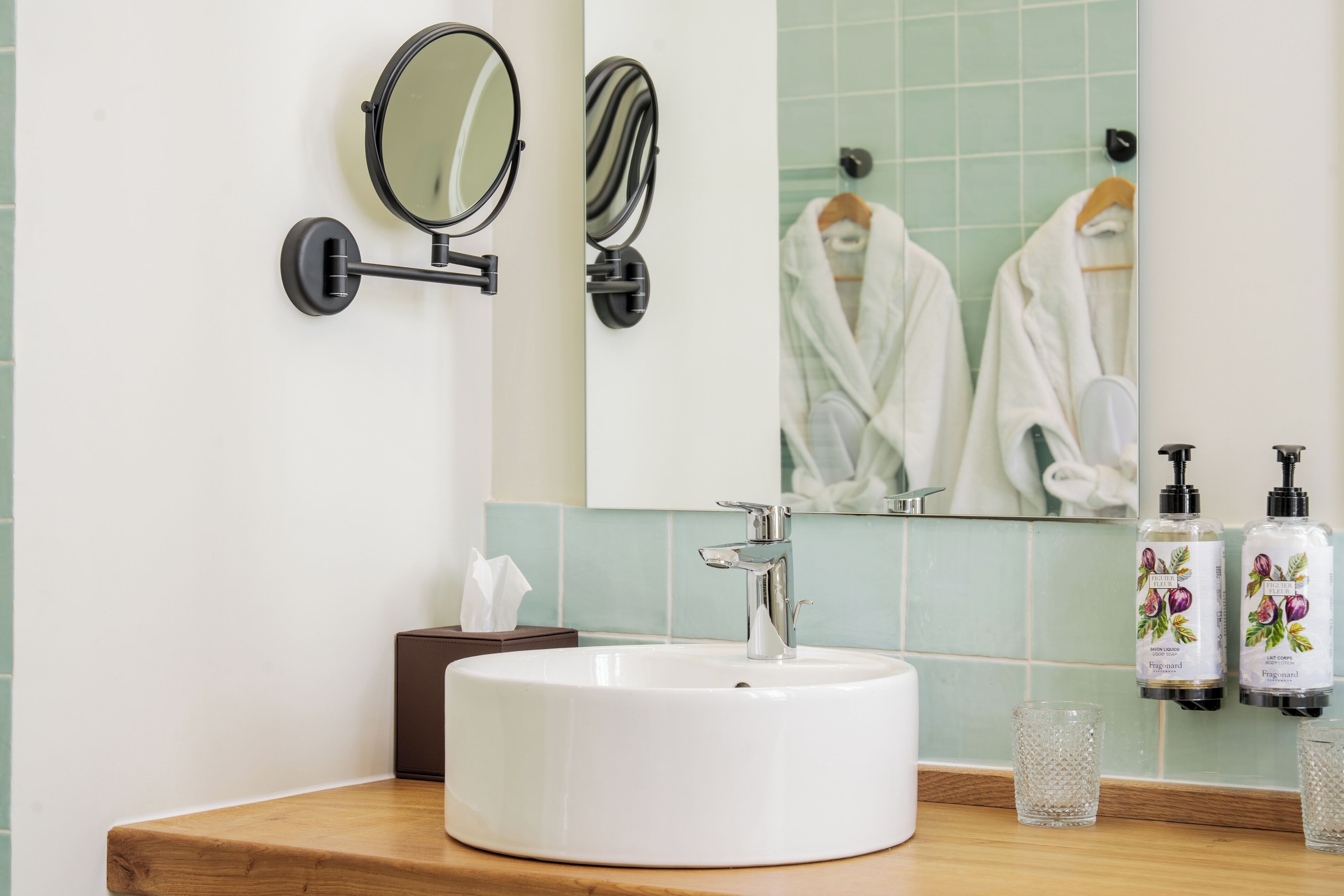 A bathroom with a white sink, two wall-mounted mirrors, a large mirror, and two bottles of hand soap.