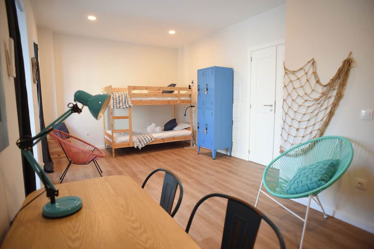 A bunk bed, a desk with a lamp, a chair, a wardrobe, and a hammock.