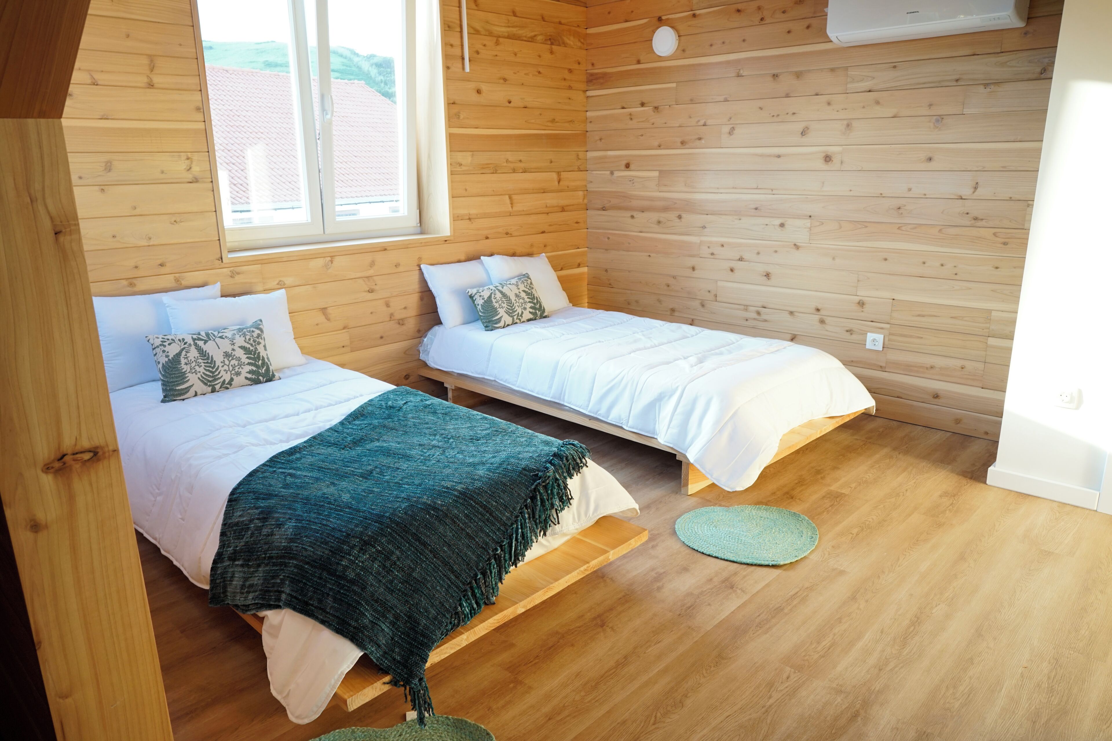 Una habitación con dos camas, paredes de madera, una ventana y un ventilador de techo.