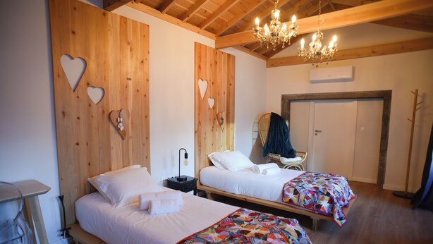 A room with two beds, wooden walls, a chandelier, and a door. - largobispohostel (Horta)