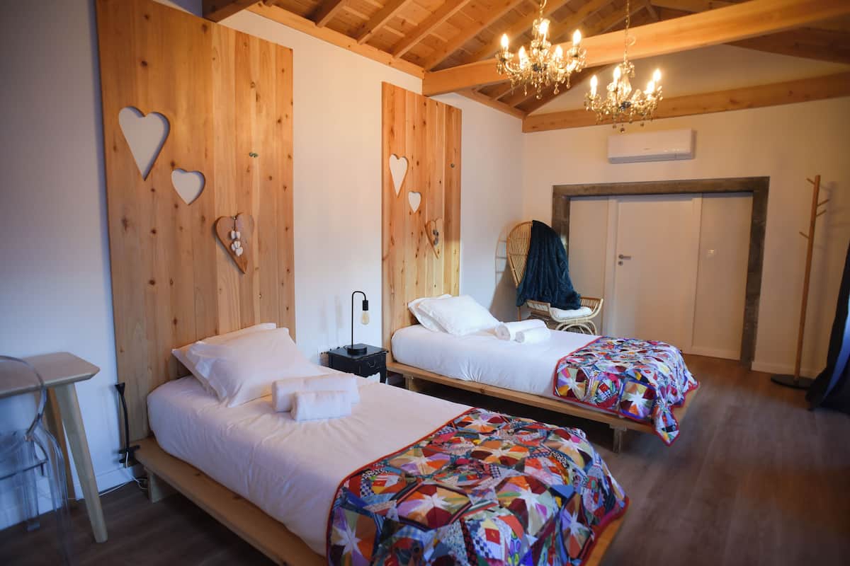A room with two beds, wooden walls, a chandelier, and a door.