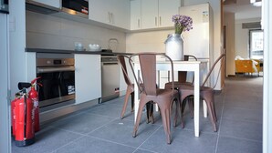 A modern kitchen with white cabinets, stainless steel appliances, and a dining area with brown chairs and a vase of flowers. - largobispohostel (Horta)