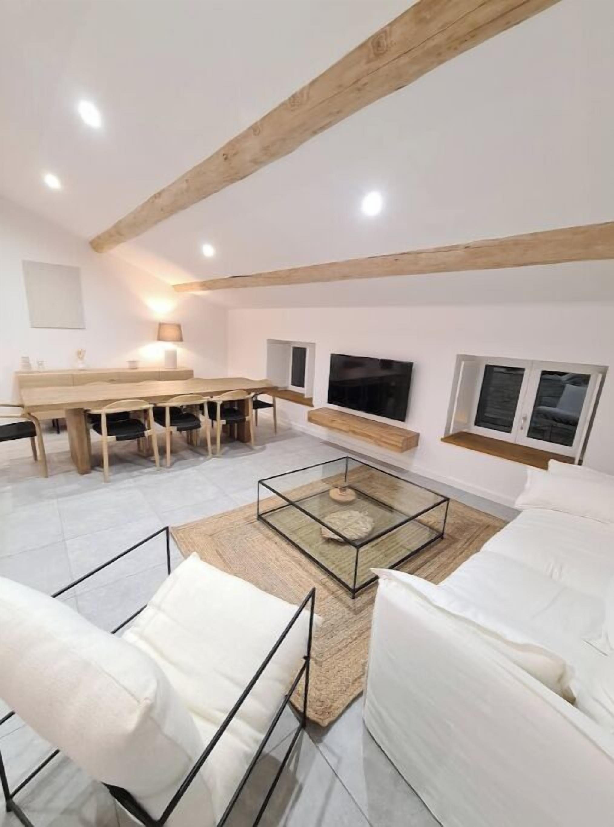 Ein modernes Wohnzimmer mit Holzboden, einem Glastisch, weißen Sofas und einem Essbereich mit Holztisch und Stühlen.