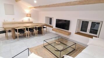 Ein modernes Wohnzimmer mit Holzboden, einem Glastisch, weißen Sofas und einem Essbereich mit Holztisch und Stühlen.