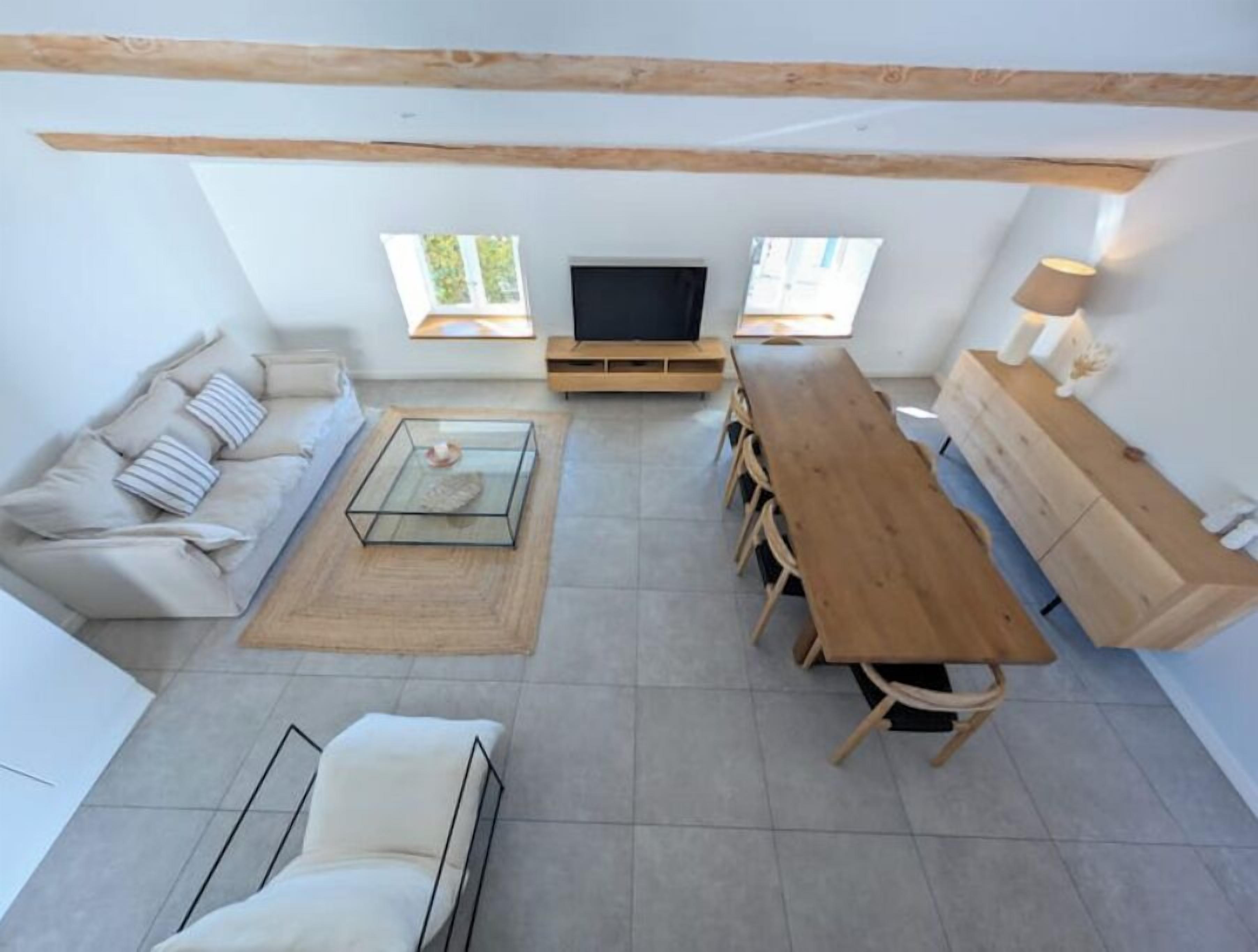 Een moderne woonkamer met een bank, een glazen salontafel, een houten eettafel en een televisie.