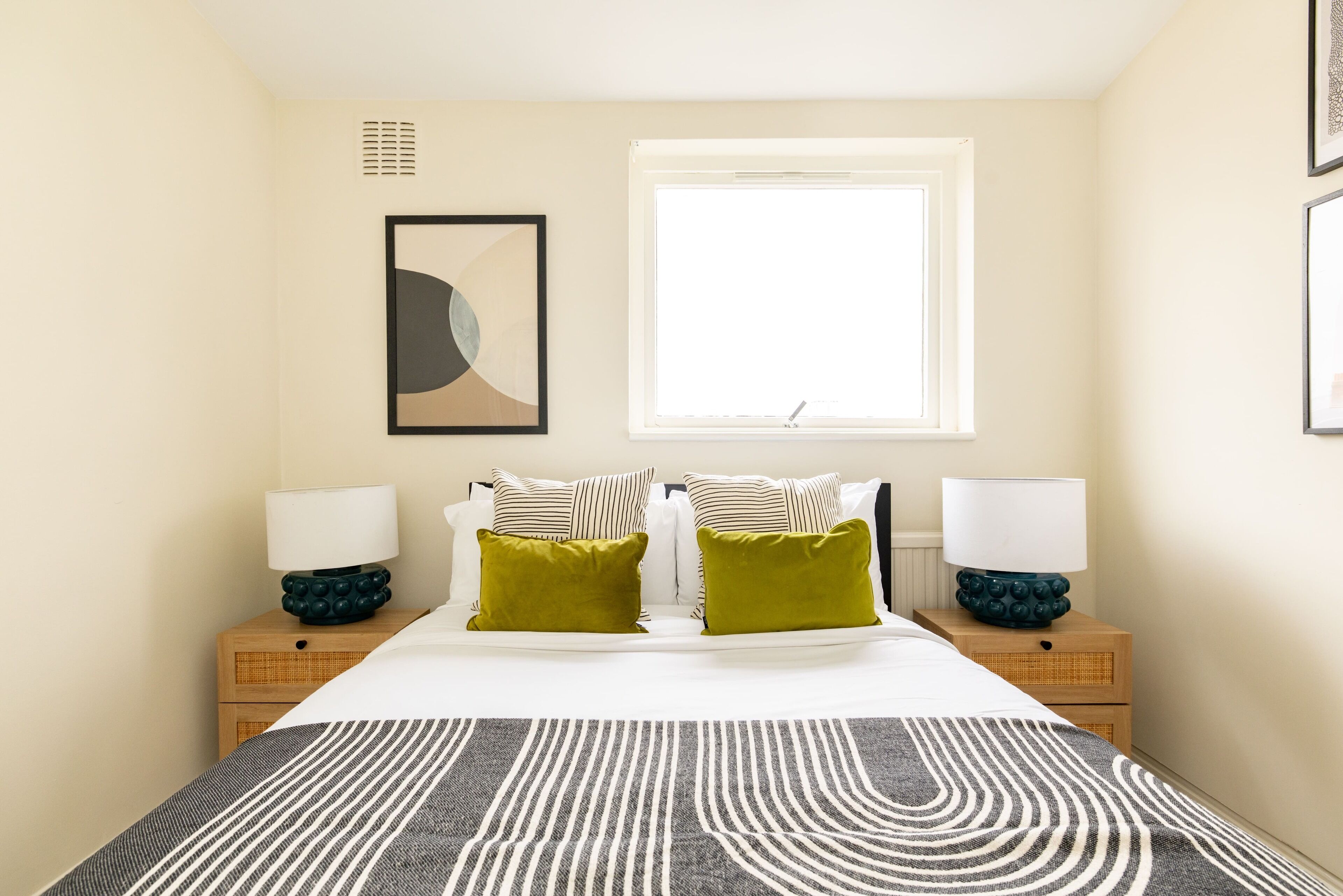 Un dormitorio con una cama, dos mesitas de noche, un ventanal y un cuadro abstracto colgado en la pared.
