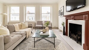 A living room with a sofa, chairs, a coffee table, a fireplace, and large windows. - Stylish West Kensington Duplex (London)