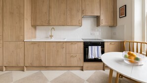 A modern kitchen with wooden cabinets, a white countertop, and a black oven. - Stylish West Kensington Duplex (London)