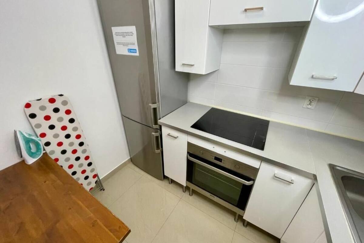 Eine kleine Küche mit weißen Schränken, einem Edelstahl-Kühlschrank, einem eingebauten Ofen und einer schwarzen Arbeitsplatte.