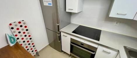 Een compacte keuken met witte kastjes, een roestvrijstalen koelkast, een inbouwoven en een zwart aanrecht.