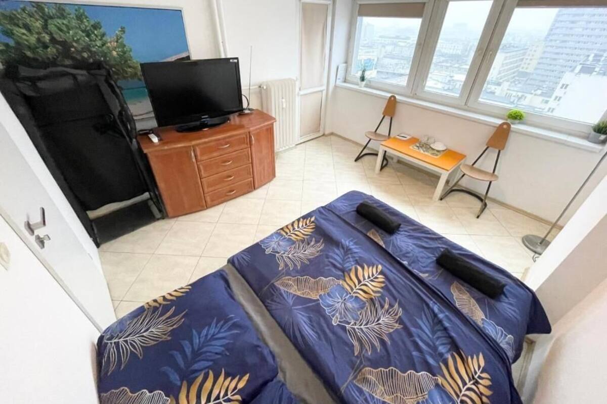Ein Schlafzimmer mit Bett, Schreibtisch, Stuhl, Fernseher und Fenster mit Blick auf die Stadt.
