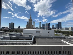 Un paisaje urbano con edificios modernos, incluyendo una torre destacada con aguja, y un edificio de techo plano en primer plano.