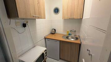 A compact kitchen with white tiles, a microwave, a sink, and wooden cabinets.
