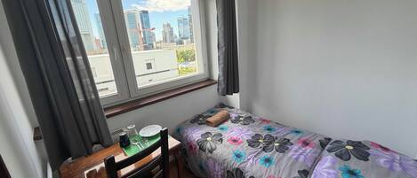 A small bedroom with a single bed, a wooden desk, and a window with curtains.