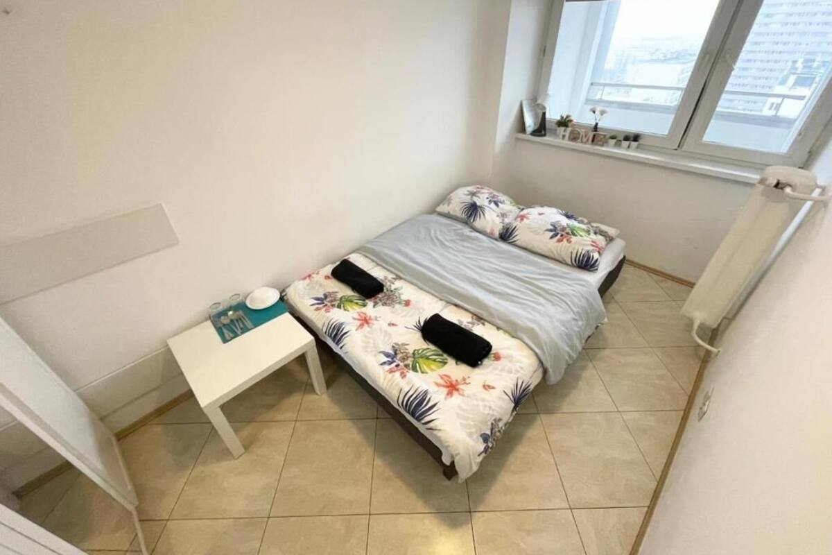 Ein kleines, gut beleuchtetes Schlafzimmer mit Bett, Nachttisch und Fenster.