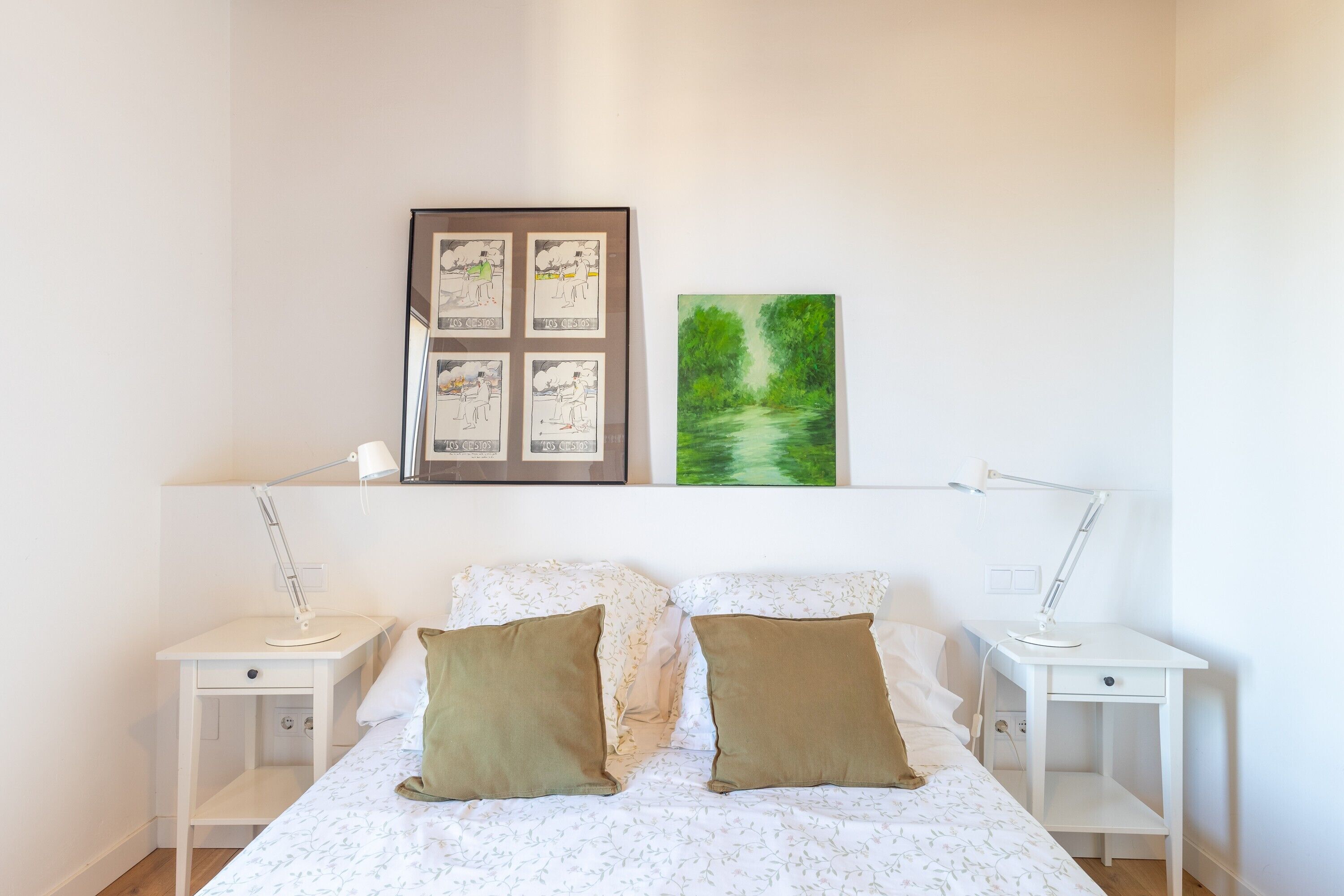 Una camera da letto con un letto, due comodini, una scrivania, una mensola con cornici e una lampada.
