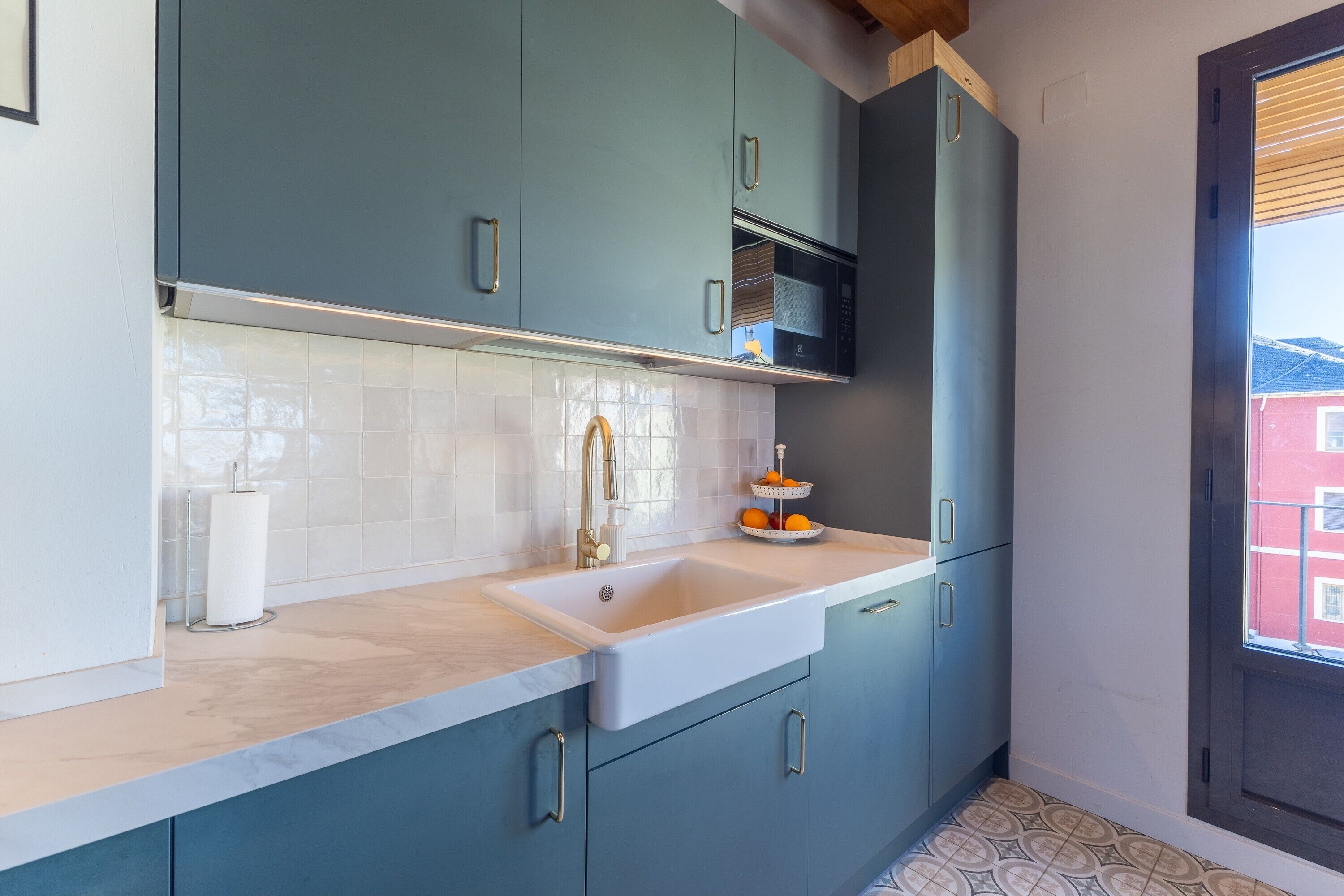 A kitchen with teal cabinets, a white sink, and a window with a view of buildings.