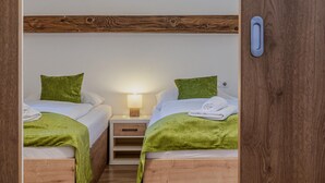 Una habitación con dos camas, cada una con una manta y almohada verdes, una mesita de noche con lámpara y un cabecero de madera.