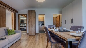 Una sala de estar moderna con un sofá, una mesa de comedor para dos personas y una cocina al fondo.