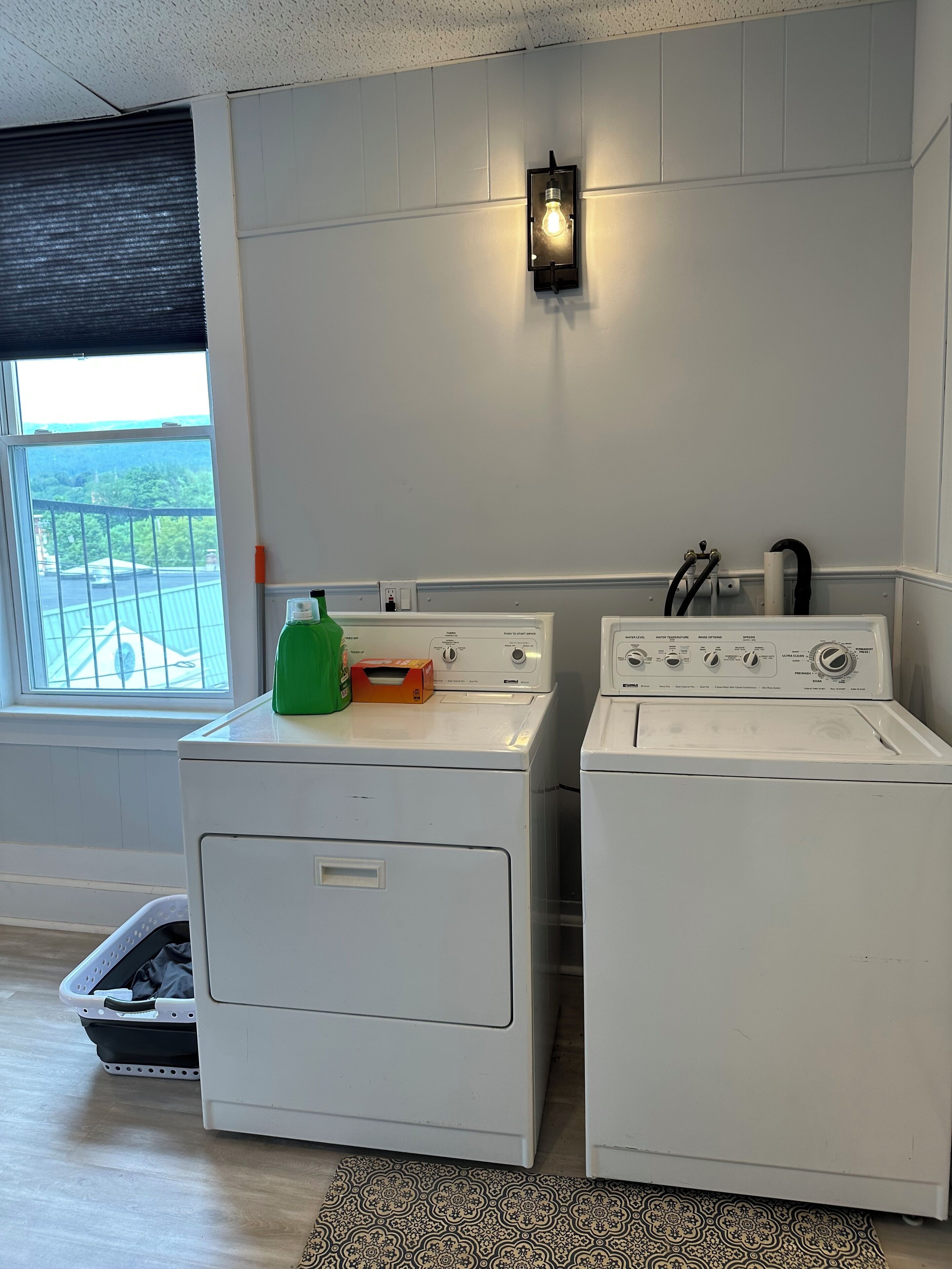 A laundry room with two white washing machines, a green bottle, and a black hose.