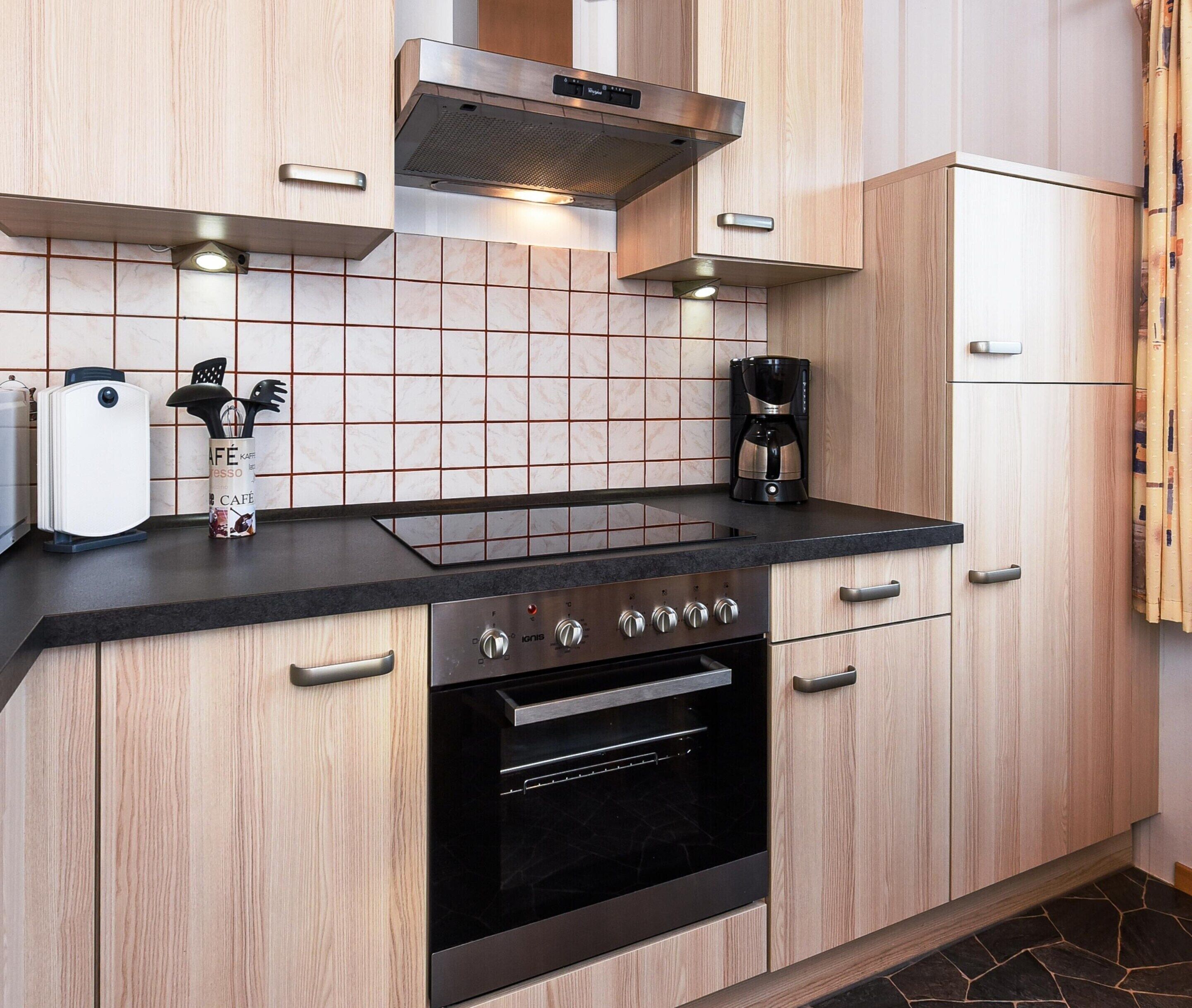 A modern kitchen with a black countertop, stainless steel appliances, and wooden cabinetry.