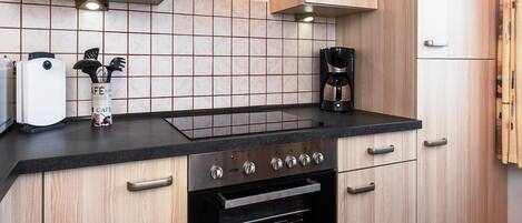 A modern kitchen with a black countertop, stainless steel appliances, and wooden cabinetry.