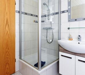 A glass-enclosed shower with a handheld showerhead, a white sink with a soap dispenser, and a wooden door. - Ferienwohnung fur bis zu 3 Personen in Bensersiel (Esens)