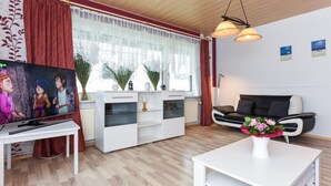 A modern living room with a white sofa, a coffee table, a TV, and a window with curtains. - Ferienwohnung fur bis zu 3 Personen in Bensersiel (Esens)