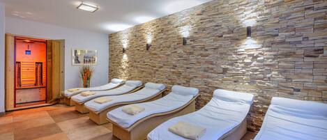A spa room with four reclining beds, a stone wall, and a wooden door leading to a sauna area.