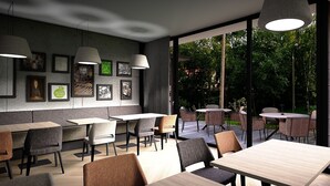 L’intérieur d’un restaurant moderne, avec des tables et des chaises en bois, des luminaires suspendus, des œuvres d’art encadrées accrochées aux murs et une vue sur la terrasse extérieure.
