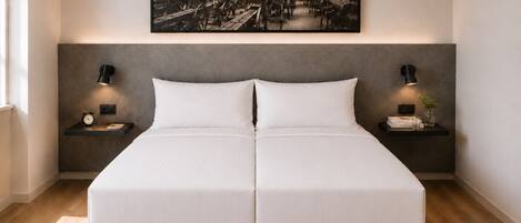 A double bed with a grey headboard, two bedside tables with lamps, a clock, and a framed picture above.