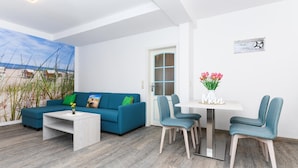 A modern living room with a blue sofa, a white coffee table, and teal chairs around a small white table. - Komfortable Ferienwohnung mit Terrasse; Bensersiel (Esens)