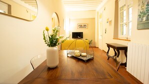 Un comedor con una mesa de madera, un jarrón con flores, un sofá amarillo y un televisor al fondo.