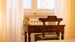 Una silla de madera con un cojín de cuadros frente a una ventana con cortinas ligeras.