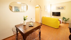 Un comedor con una mesa de madera, sillas transparentes, un florero con flores y un sofá amarillo al fondo.