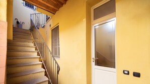 Una escalera que lleva a una puerta con ventana, una planta pequeña en maceta y un interruptor de luz en la pared.