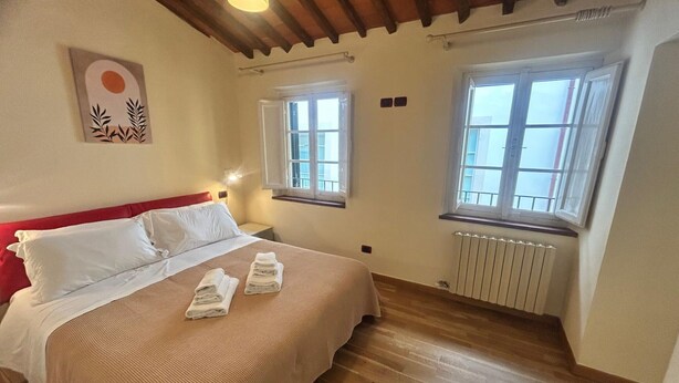A bedroom with a bed, two windows, a radiator, and a wall art piece. - Owl Palace, Royal Owl in Center Town (Lucca)