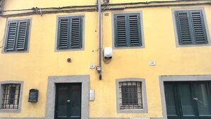 A yellow building with numbered doors and windows, featuring a simple facade and a metal vent. - Owl Palace, Royal Owl in Center Town (Lucca)