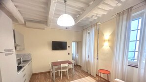 Ein kompakter Wohnbereich mit Küchenzeile, Essbereich, Sofa und Wand-Fernseher.