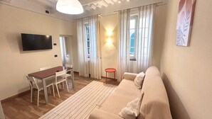 Ein Wohnzimmer mit einer Couch, einem an der Wand montierten Fernseher, einem Esstisch mit Stühlen und einem kleinen Beistelltisch.