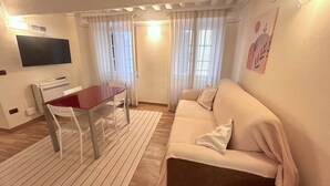 Una sala de estar con sofá, televisor, mesa de comedor y ventana con cortinas.
