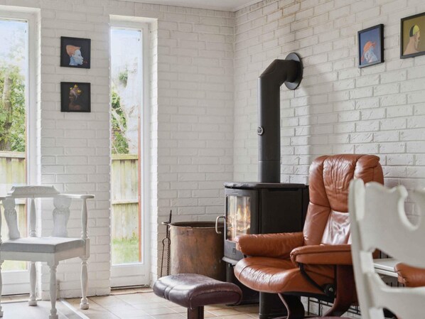 A cozy room with a white brick wall, a large window, a leather chair, and a wood-burning stove.