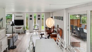 Een moderne woonkamer met een flatscreen televisie, een eethoek met een tafel en stoelen, en een groot raam met uitzicht op een tuin.
