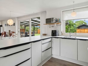 A modern kitchen with white cabinets, a black countertop, and a built-in microwave. There is a dining area with chairs and a table visible through an open doorway.